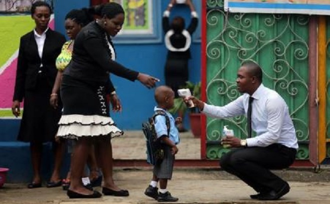 A school official takes a pupil"s temperature using an infrared digital laser thermometer in front of the school premises, at the resumption of private schools, in Lagos in this September 22, 2014 file photo.  REUTERS/Akintunde Akinleye 